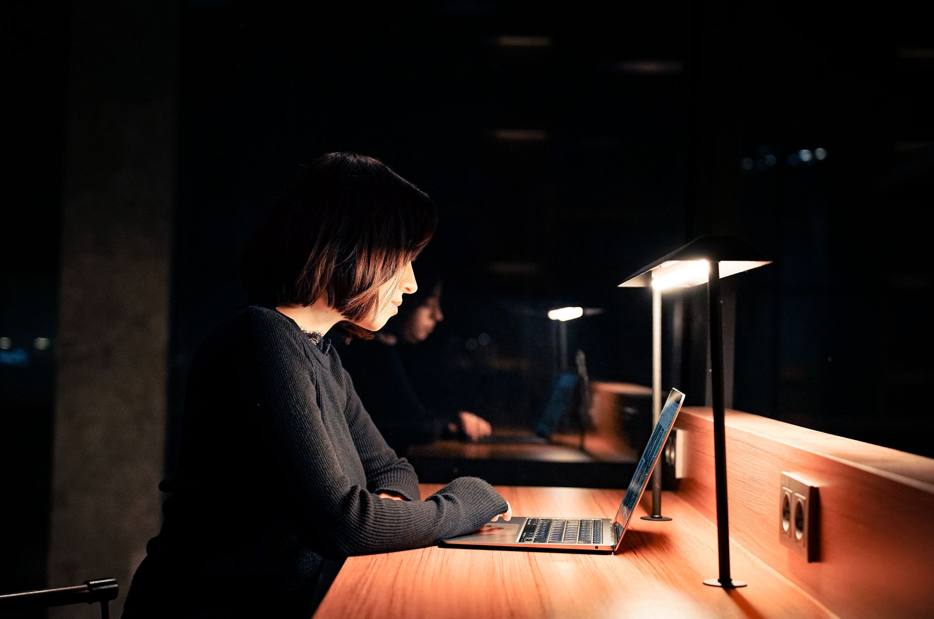 Vrouw werkt 's avonds aan een laptop aan een bureau, verlicht door een bureaulamp